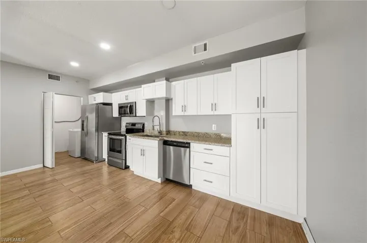 Kitchen featuring white cabinetry, appliances with stainless steel finishes, light wood-style flooring, recessed lighting, and light stone counters