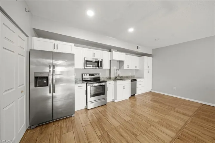 Kitchen with appliances with stainless steel finishes, white cabinets, wood tiled floors, light stone countertops, and recessed lighting