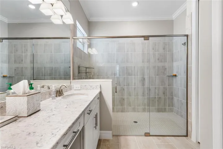 Bathroom with tile patterned floors, a shower with shower door, ornamental molding, and vanity