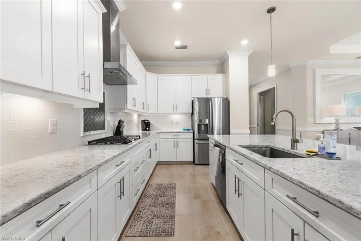 Kitchen with white cabinetry, sink, wall chimney exhaust hood, and light stone counters