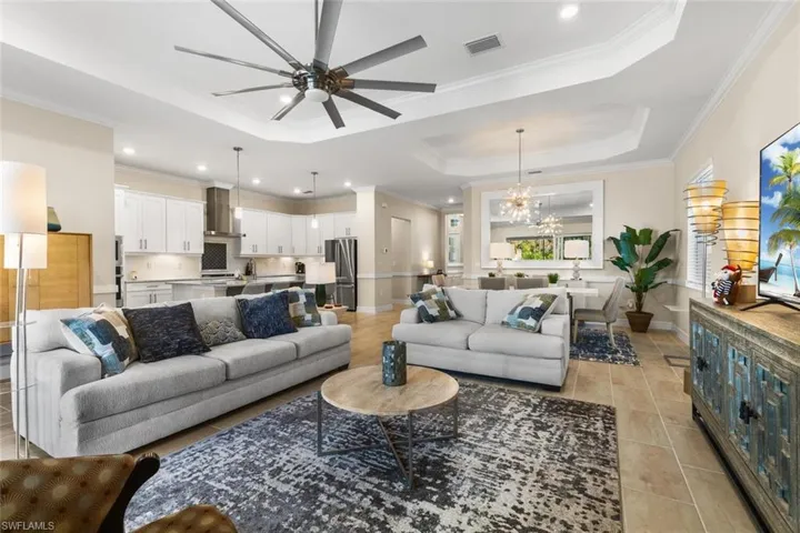 Tiled living room featuring a tray ceiling, crown molding, and ceiling fan with notable chandelier