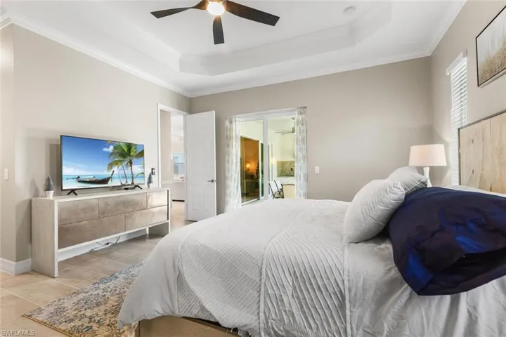 Tiled bedroom with a tray ceiling, ceiling fan, and ornamental molding