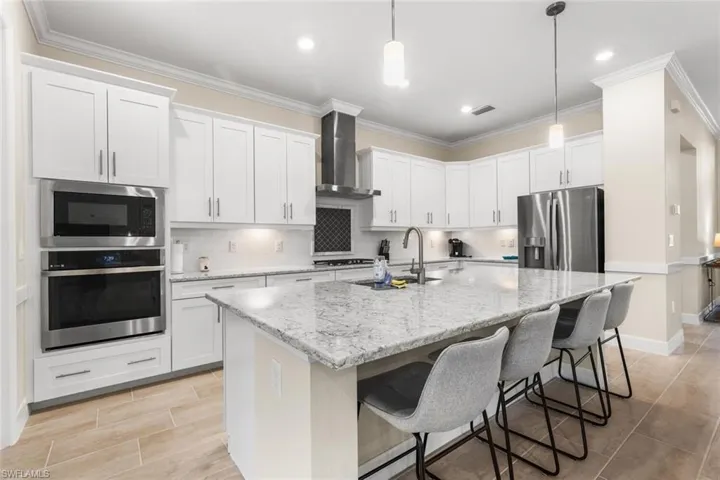 Kitchen with sink, stainless steel appliances, wall chimney range hood, a center island with sink, and white cabinets