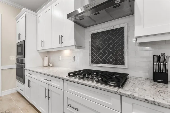 Kitchen with white cabinets, light stone countertops, extractor fan, and stainless steel gas cooktop