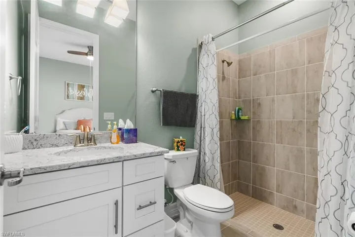 Bathroom with ceiling fan, curtained shower, vanity, and toilet
