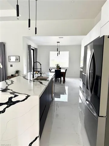 Kitchen featuring modern cabinets, decorative light fixtures, stainless steel fridge with ice dispenser, and light marble finish floors