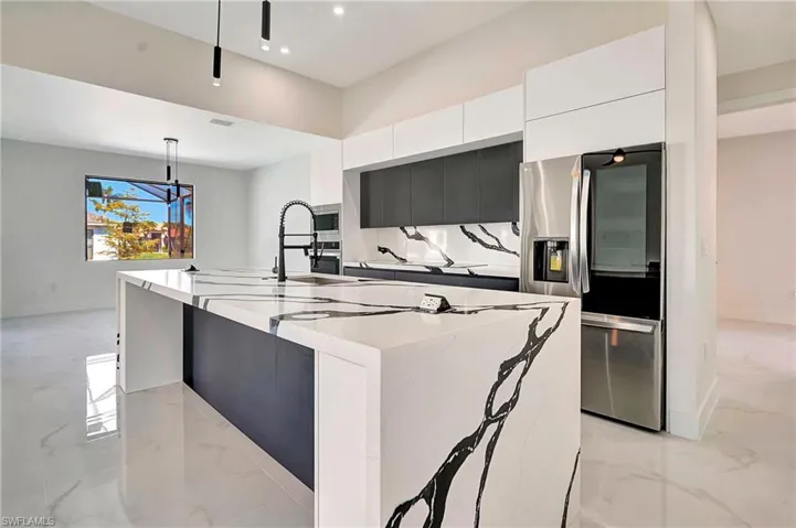 Kitchen featuring light marble finish flooring, stainless steel appliances, dark cabinetry, hanging light fixtures, and modern cabinets