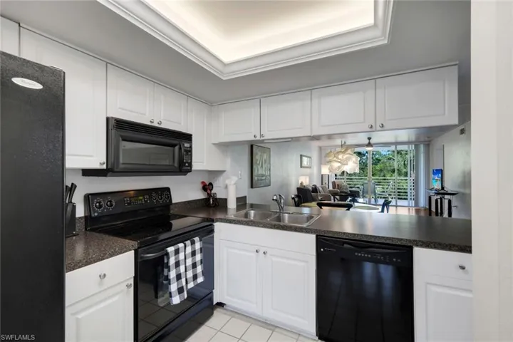 Kitchen featuring white cabinetry, dark countertops, black appliances, and a double basin stainless steel sink