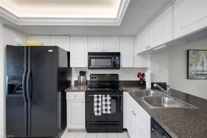 Kitchen featuring white cabinetry, dark stone-finish countertops, and black appliances