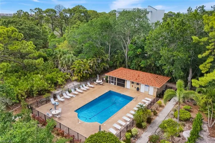 Outdoor swimming pool surrounded by a paved deck, a pool house with a red tile roof, and extensive landscaping