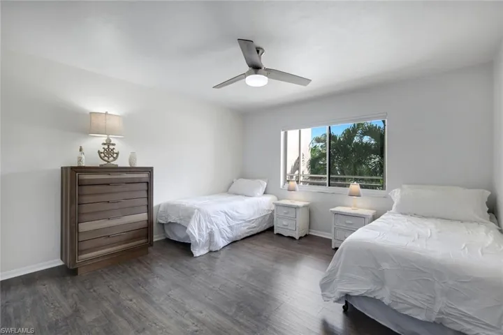 Bright room featuring wood-finish flooring, a ceiling fan with integrated lighting, and a large window overlooking exterior foliage