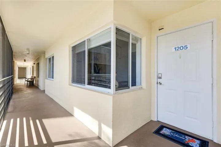 Entryway featuring a white paneled door with numeric address, neutral stucco exterior, and a screened window