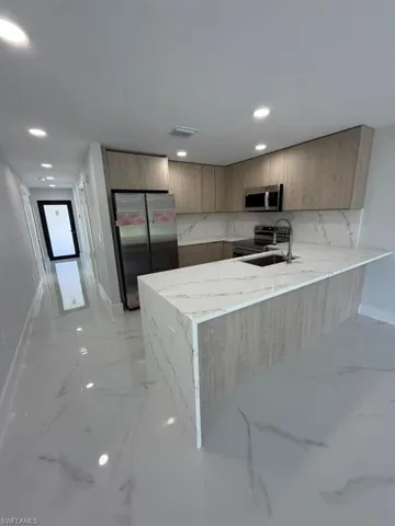 Modern kitchen featuring a waterfall island with a stone-finish countertop, wood-finish cabinetry, stainless steel appliances, and recessed lighting
