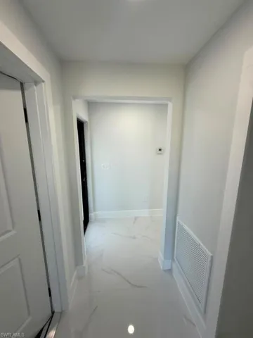 Hallway featuring white paint, white trim, and white tile flooring with subtle veining