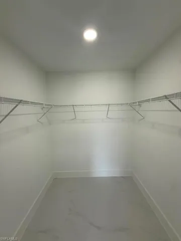 Spacious walk-in closet featuring white wire shelving, recessed lighting, white baseboards, and light-toned tile flooring with subtle veining