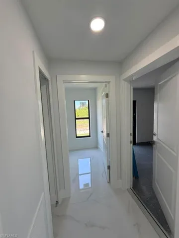 Hallway featuring white walls, recessed ceiling lighting, and white tile flooring with grey veining