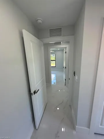 Hallway featuring large format marble-look tile flooring, white interior doors with dark hardware, and clean white baseboards