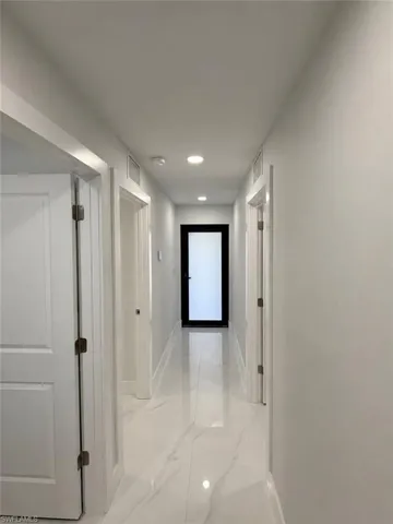 Hallway featuring white marble-look flooring, recessed ceiling lighting, and white baseboards