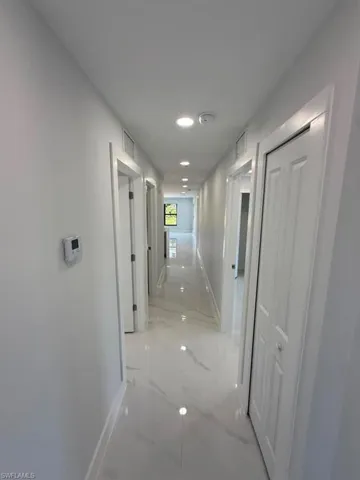 Long hallway featuring white tile flooring with gray veining, white baseboards, and white walls