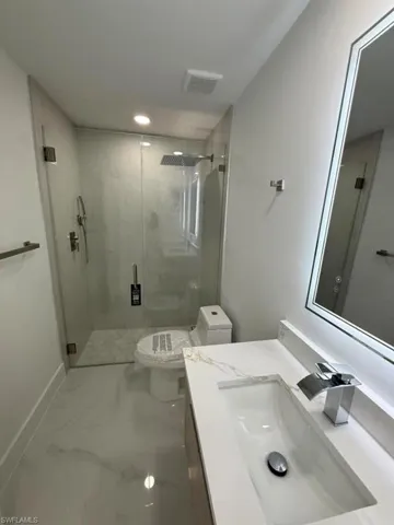 Contemporary bathroom featuring a frameless glass shower enclosure, a rainfall showerhead, a modern vanity with integrated sink, a rectangular illuminated mirror, and large format tile flooring