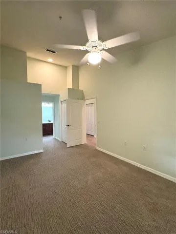 Unfurnished room with a high ceiling, ceiling fan, and dark colored carpet