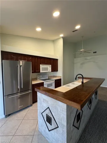 Kitchen featuring white appliances, dark wood finish cabinets, butcher block countertops, ceiling fan, and an island with sink