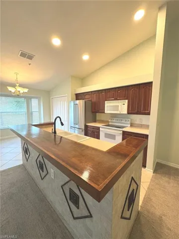 Kitchen with butcher block counters, light carpet, lofted ceiling, white appliances, and light tile patterned flooring