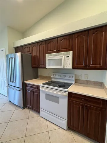 Kitchen with white appliances, light countertops, lofted ceiling, dark wood finish cabinetry, and light tile patterned floors