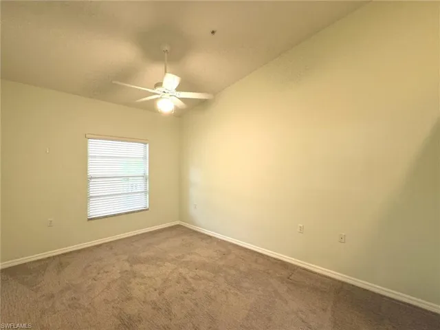 Carpeted empty room with lofted ceiling and a ceiling fan