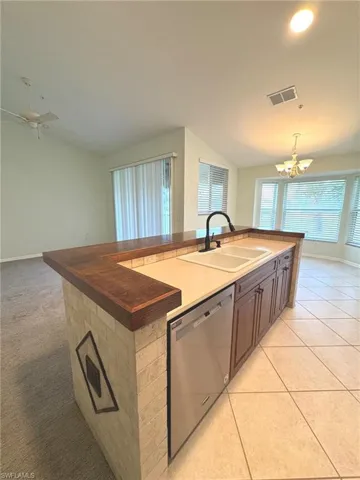 Kitchen featuring an island with sink, a chandelier, vaulted ceiling, stainless steel dishwasher, and wooden counters