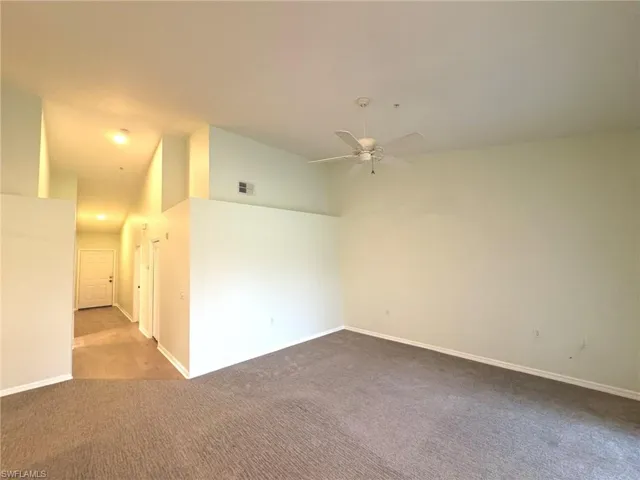 Empty room with vaulted ceiling, a ceiling fan, and dark carpet