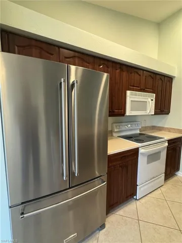 Kitchen with white appliances, light countertops, dark wood finish cabinetry, and light tile patterned floors