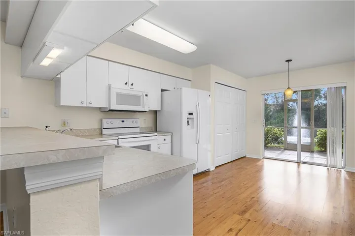 Kitchen featuring light wood-type flooring, white appliances, light countertops, white cabinetry, and pendant lighting