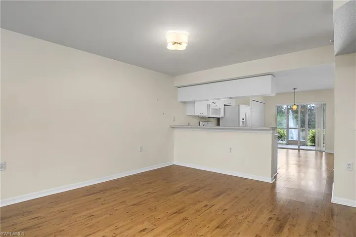 Kitchen featuring baseboards, white appliances, a peninsula, white cabinets, and wood finished floors