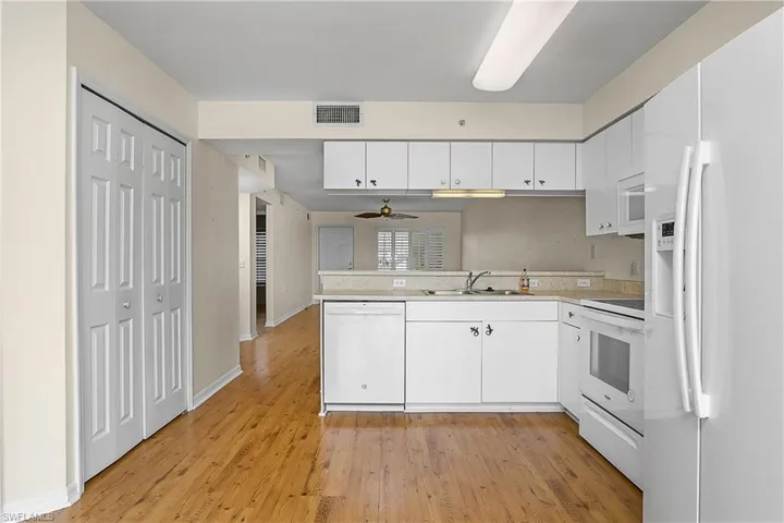 Kitchen with white appliances, a peninsula, white cabinets, visible vents, and a sink