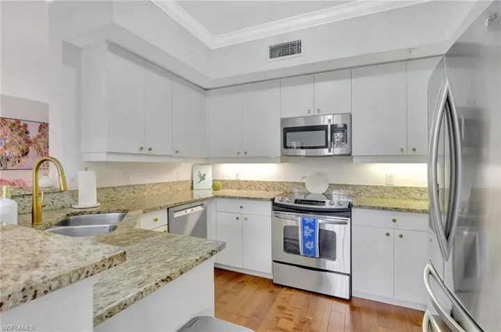 Kitchen featuring appliances with stainless steel finishes, crown molding, light stone counters, white cabinets, and sink