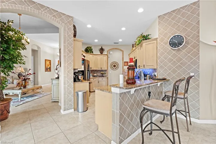 Kitchen with light tile patterned floors, kitchen peninsula, a kitchen breakfast bar, light brown cabinetry, and light stone counters