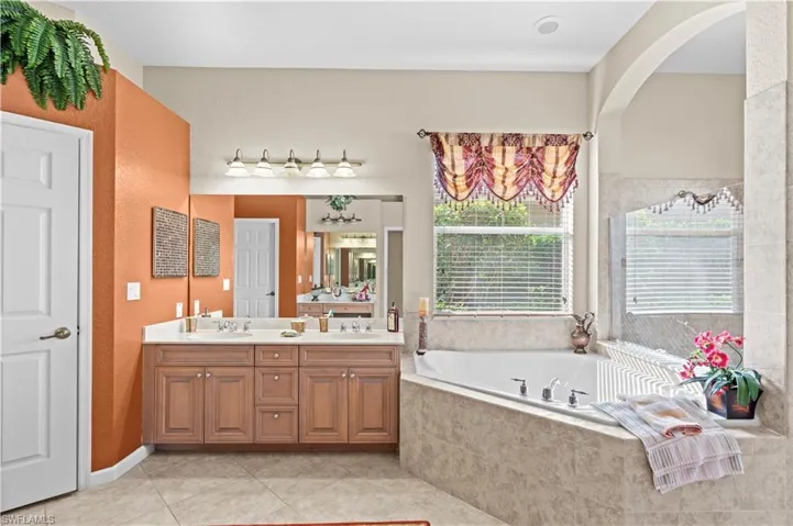 Bathroom featuring tiled tub, vanity, and tile patterned flooring