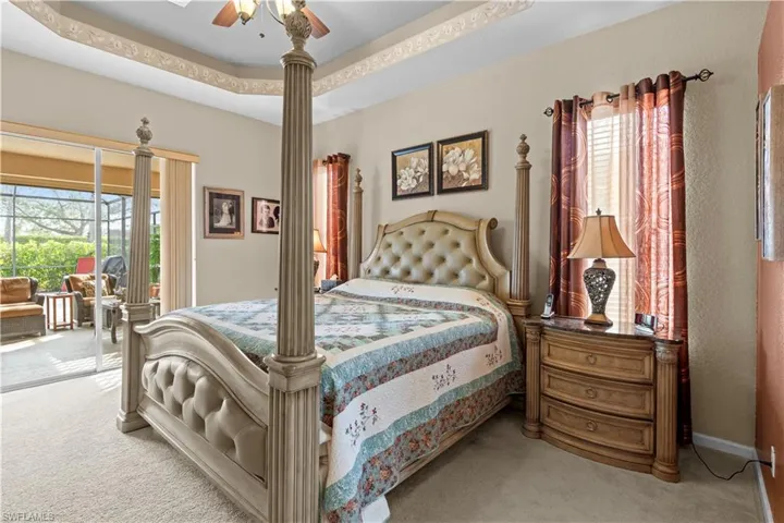 Bedroom with ceiling fan, light carpet, a tray ceiling, and multiple windows