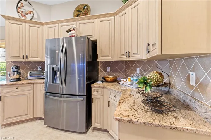 Kitchen with stainless steel refrigerator with ice dispenser, light stone counters, backsplash, and light tile patterned floors