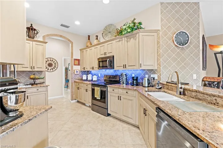 Kitchen with light tile patterned floors, stainless steel appliances, backsplash, light stone counters, and sink