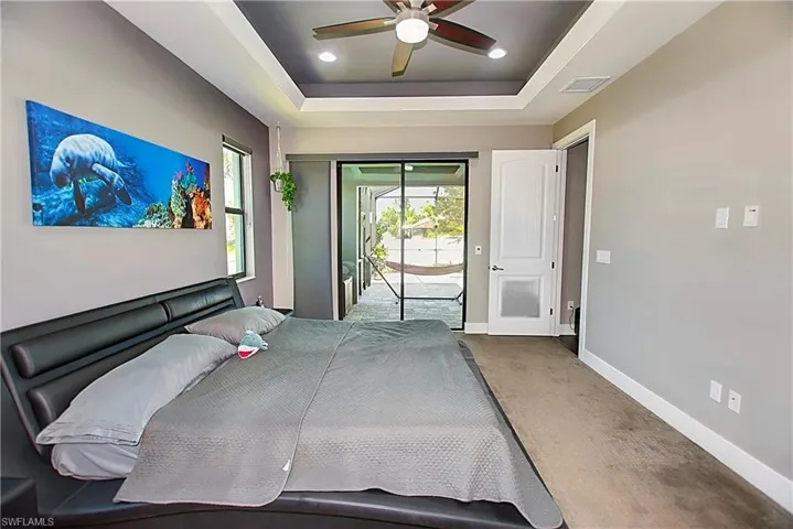 Carpeted bedroom with access to outside, a raised ceiling, and ceiling fan