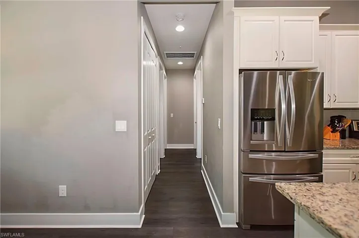 Kitchen featuring white cabinets, stainless steel fridge with ice dispenser, light stone counters, and dark wood-type flooring