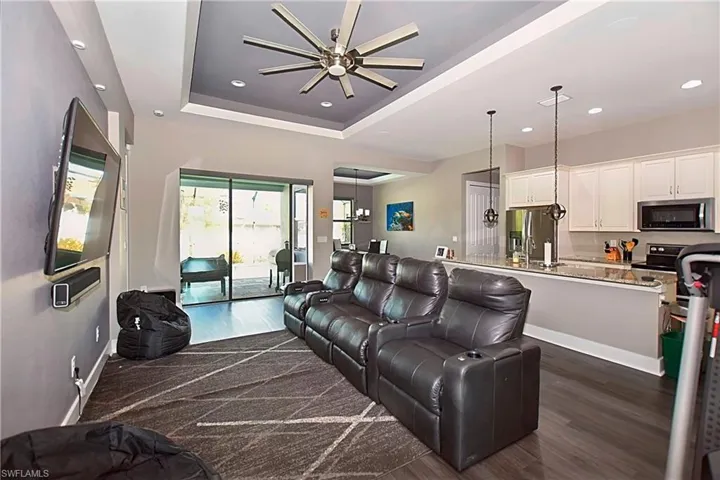 Living room featuring dark wood-type flooring, ceiling fan, and a raised ceiling