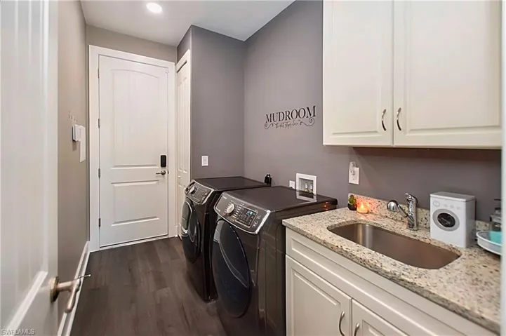 Clothes washing area with sink, cabinets, dark hardwood / wood-style floors, and washing machine and clothes dryer