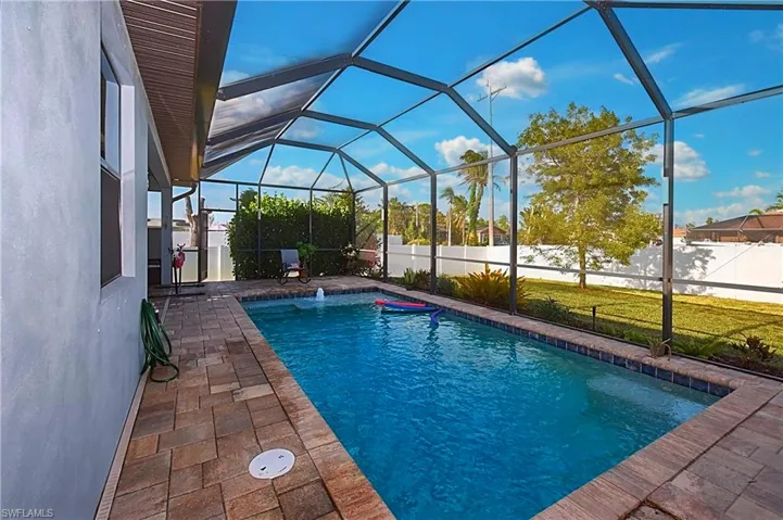 View of pool with pool water feature, glass enclosure, a patio area, and a lawn