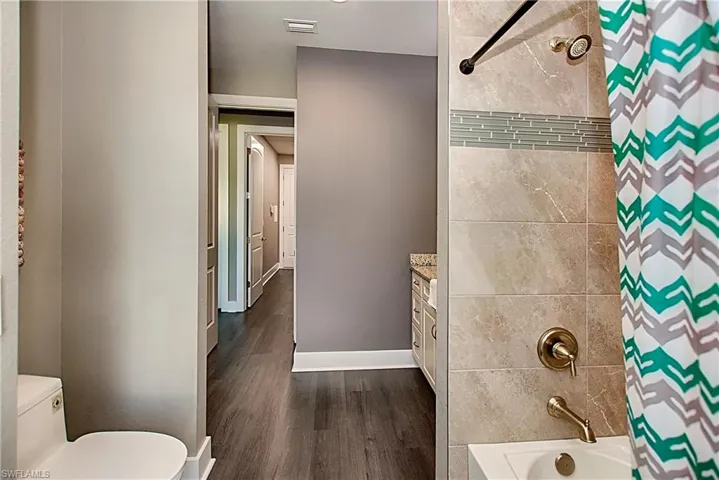 Full bathroom with wood-type flooring, toilet, vanity, and shower / tub combo with curtain
