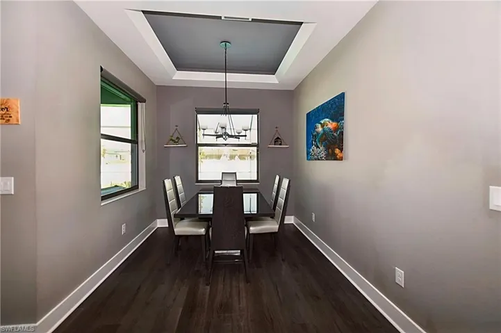 Dining area with dark hardwood / wood-style floors, a chandelier, and a tray ceiling