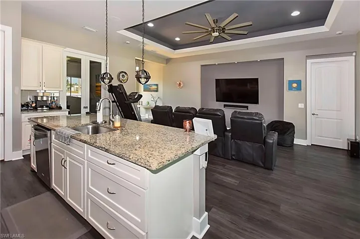 Kitchen with white cabinetry, ceiling fan, a tray ceiling, dark hardwood / wood-style floors, and a kitchen island with sink