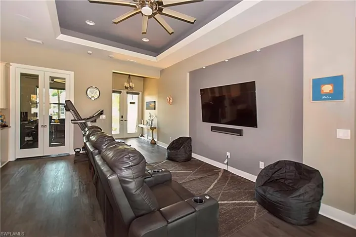 Living room with dark hardwood / wood-style floors, ceiling fan, french doors, and a tray ceiling